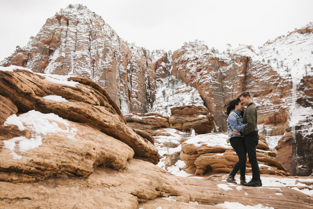 Couple snuggle close in winter in Zion National Park at a canyon overlook