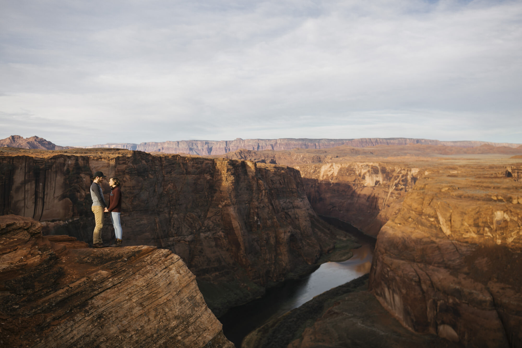 Engaged couple stand holding hands at Horseshoe Bend in Arizona at sunrise