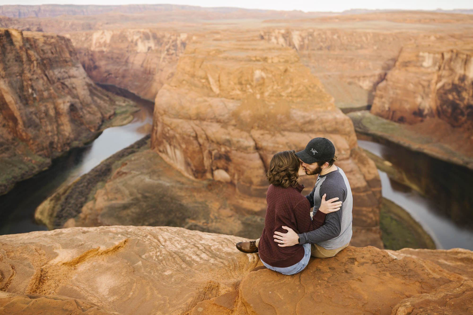 Adventure couple sit on the edge of Horseshoe Bend with the Colorado River far below