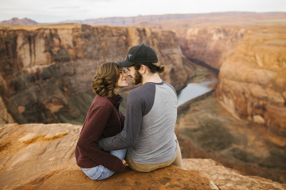 Engaged couple sit and snuggle at Horseshoe Bend outside Page Arizona