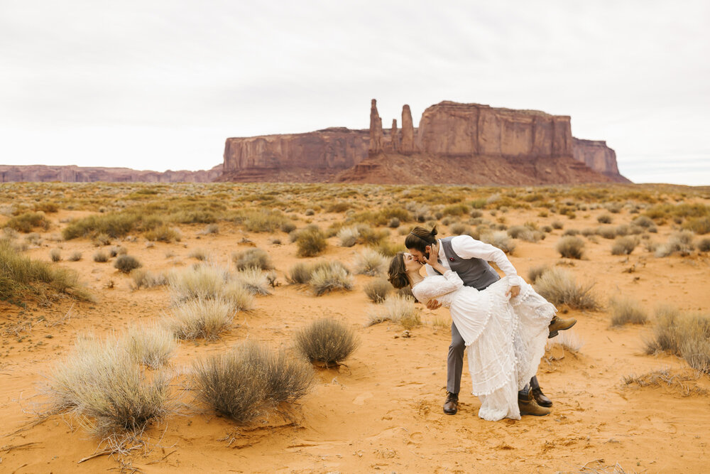 Groom dips his bride for a big kiss after their elopement wedding ceremony at their Monument Valley wedding