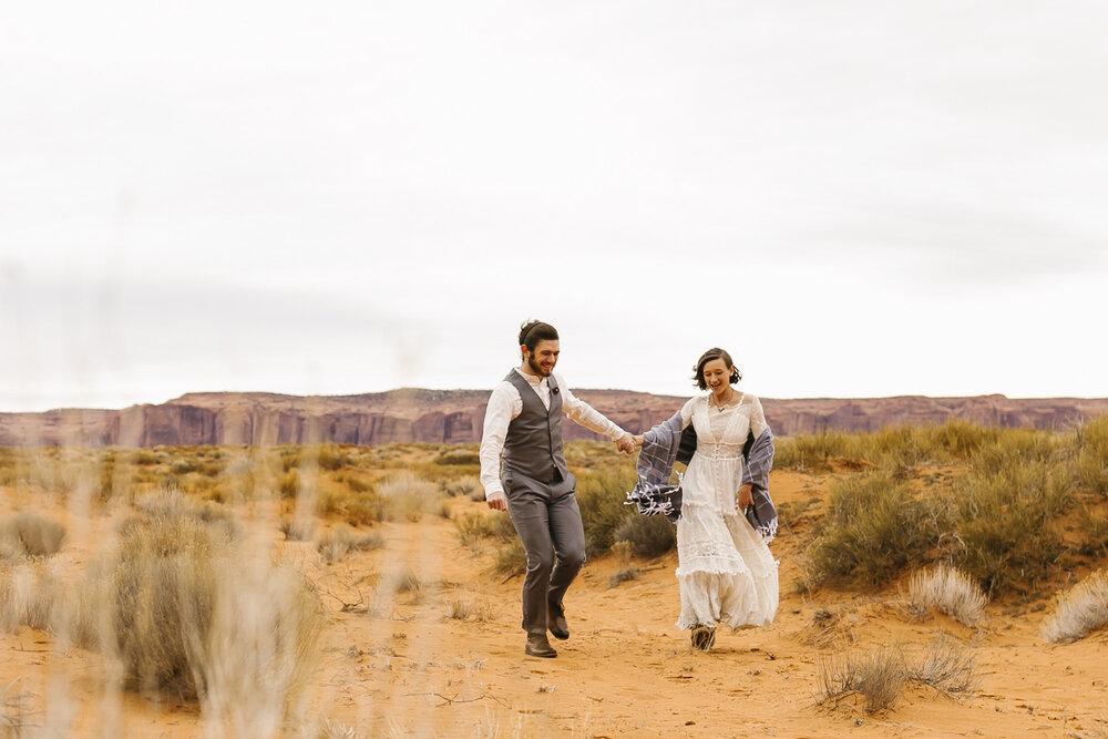 Just married couple joyfully frolic through the desert at their wedding in Monument Valley