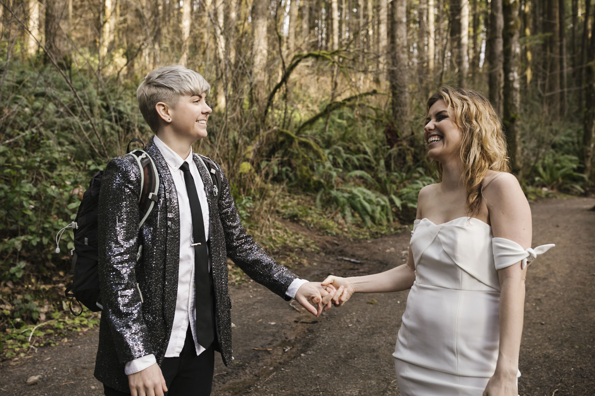 Same sex couple laugh on hiking trail in a Washington forest on their elopement day