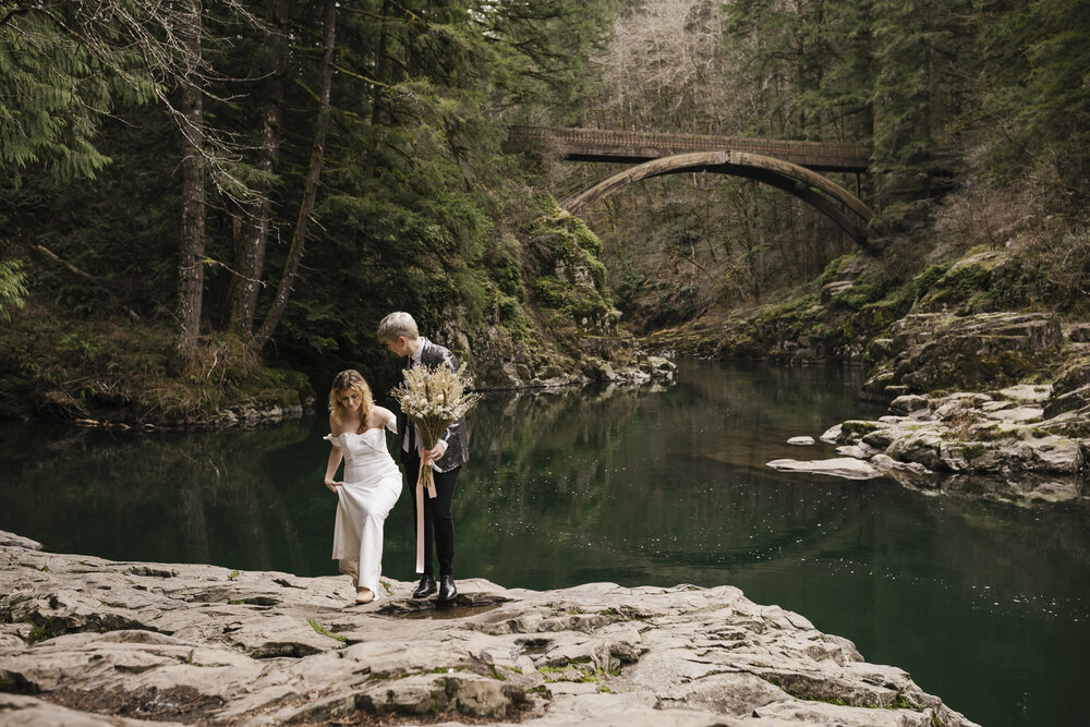 Same sex couple celebrate their elopement day in front of the bridge at Moulton Falls in Washington