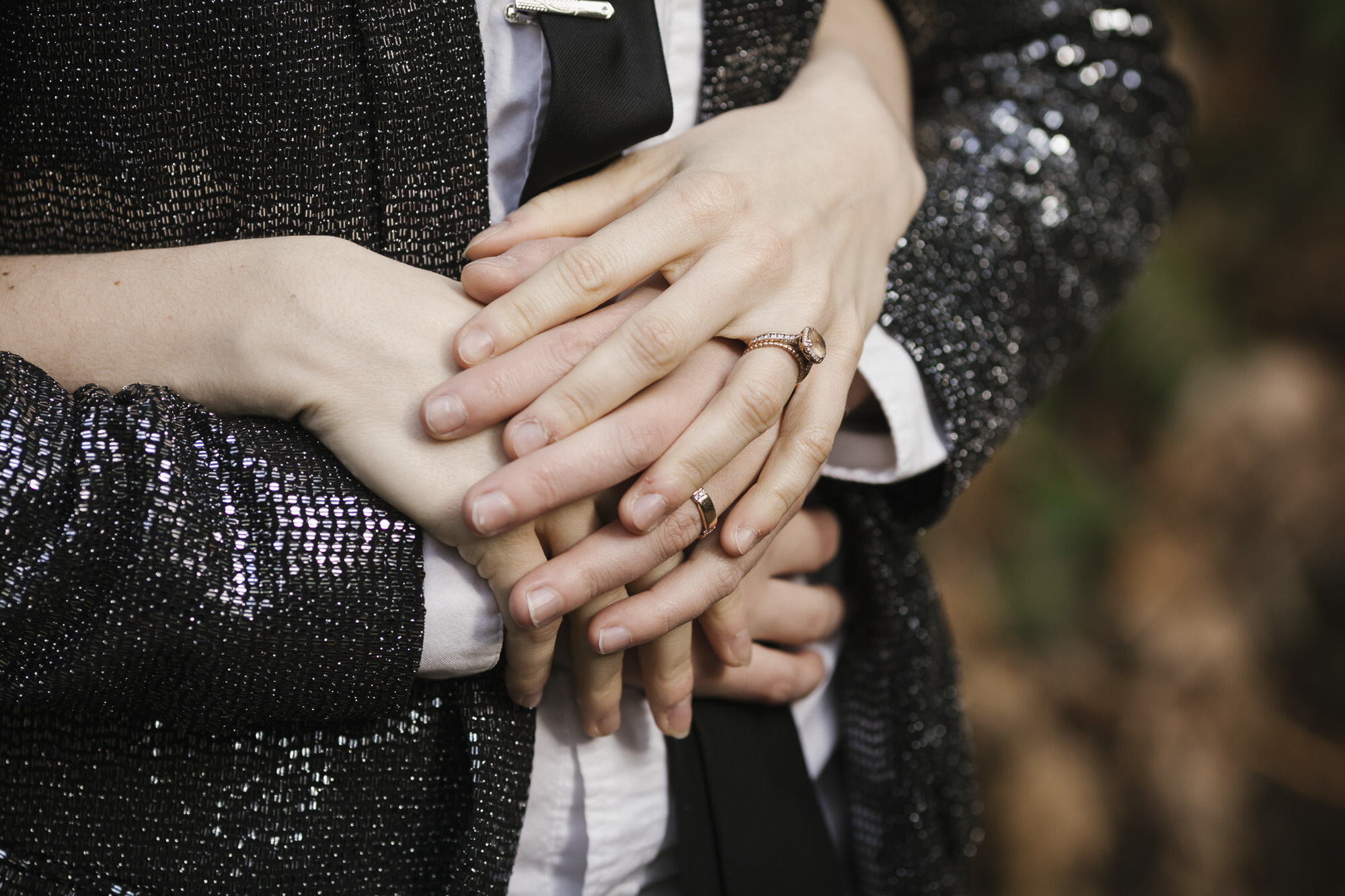 Close up of wedding couple's hands, one partner wears silver sequined sparkly jacket