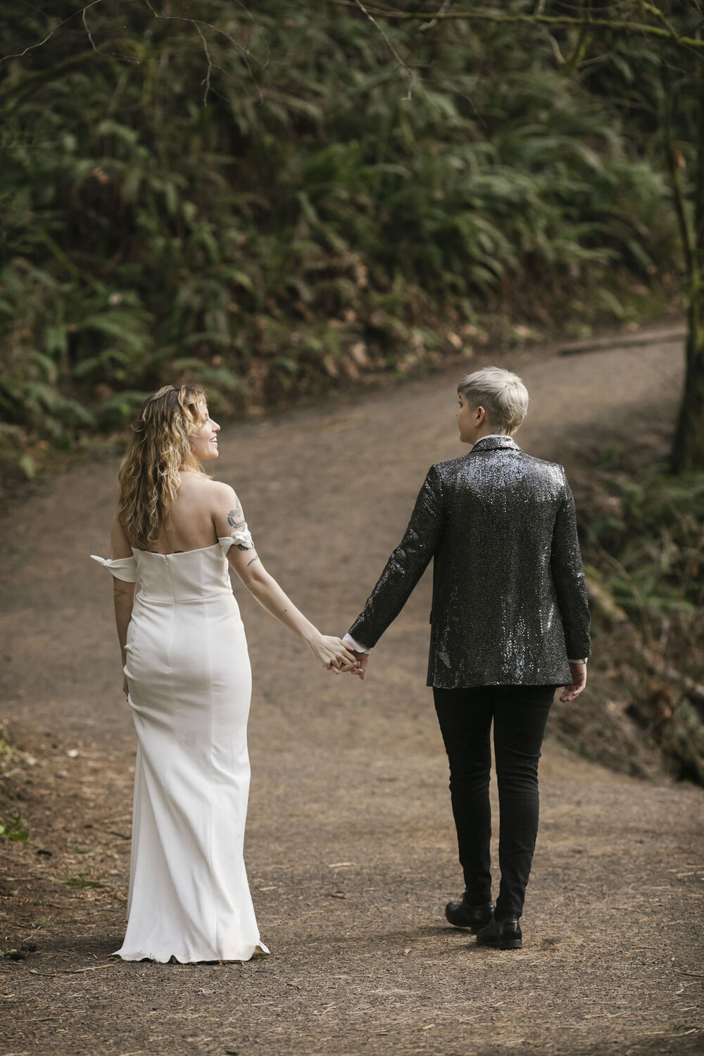 Same sex wedding couple walk holding hands through a forest in Washington