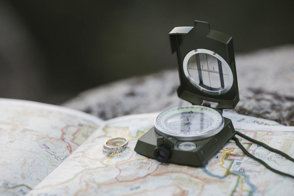 Paper map, compass, and close up shot of coordinate wedding bands during an adventurous hiking elopement