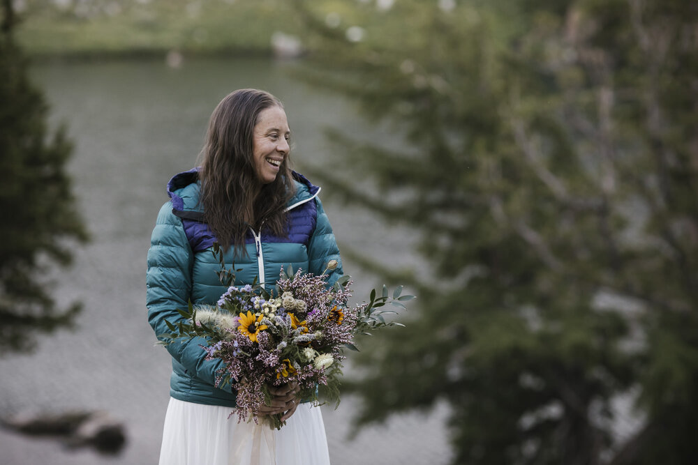 Bride in her wedding dress and puffy jacket holding her bouquet during her backpacking elopement