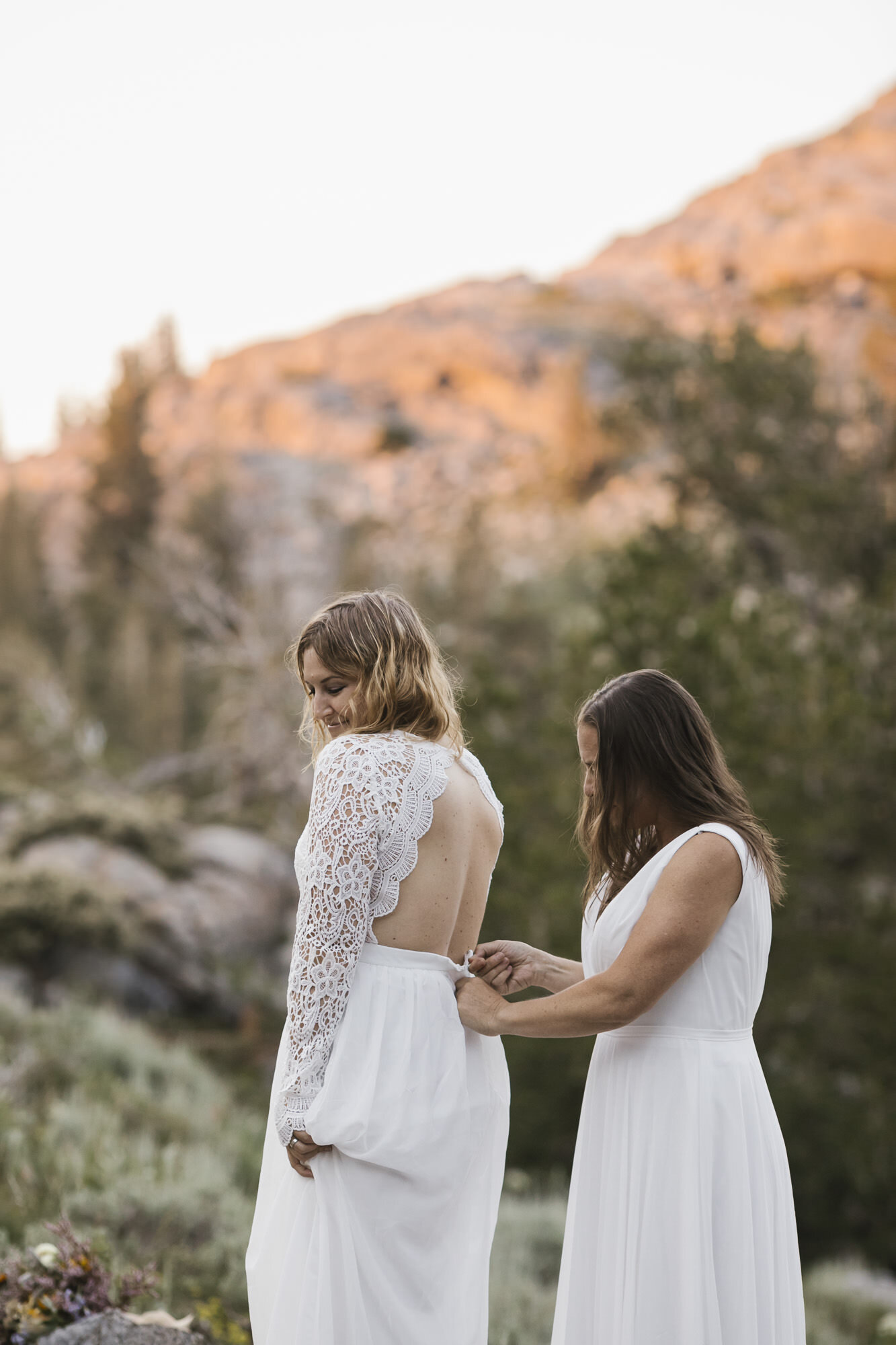 Brides help each other get dressed during their backpacking elopement in the mountains