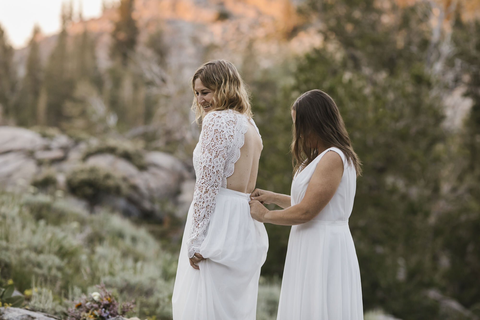 Bride helps her soon to be wife zip up her wedding dress during their adventurous hiking elopement