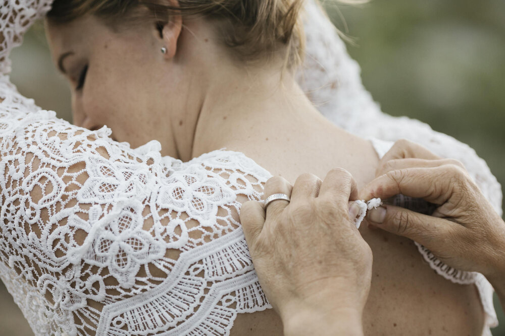 Bride helps her bride button her wedding dress