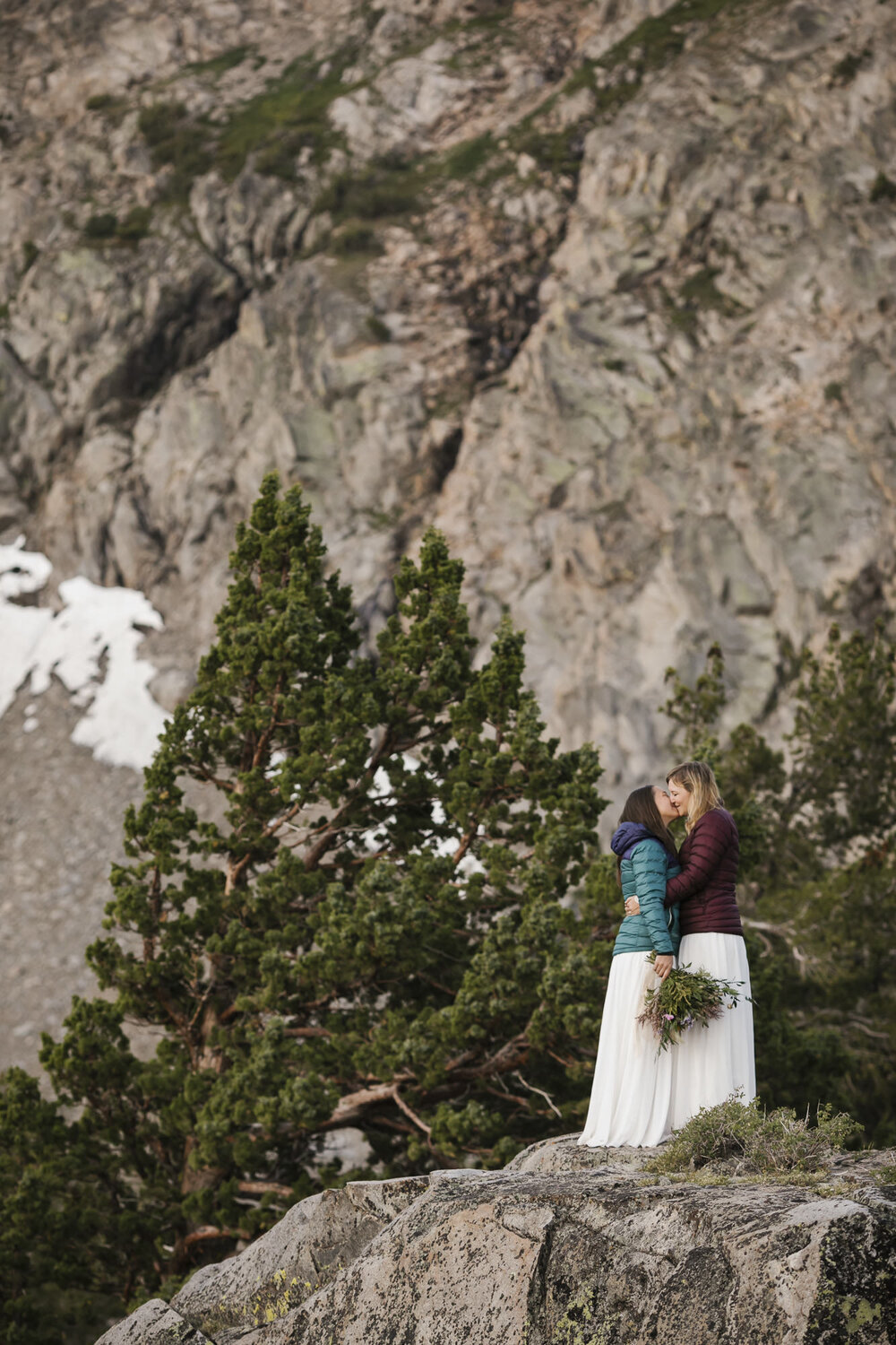 Wedding couple kiss at sunrise during their mountain elopement wearing their puffy jackets and wedding dresses
