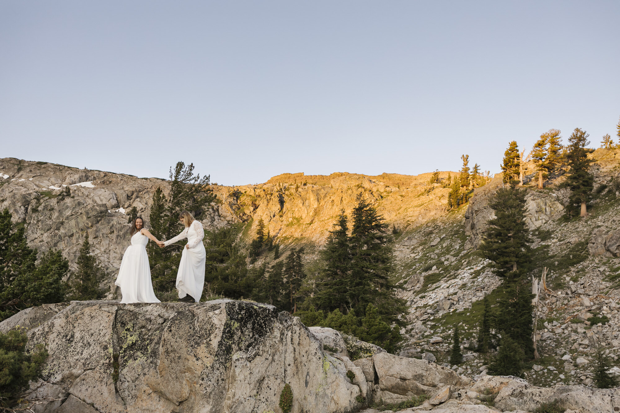 Lesbian wedding couple hold hands at sunrise during their mountain elopement
