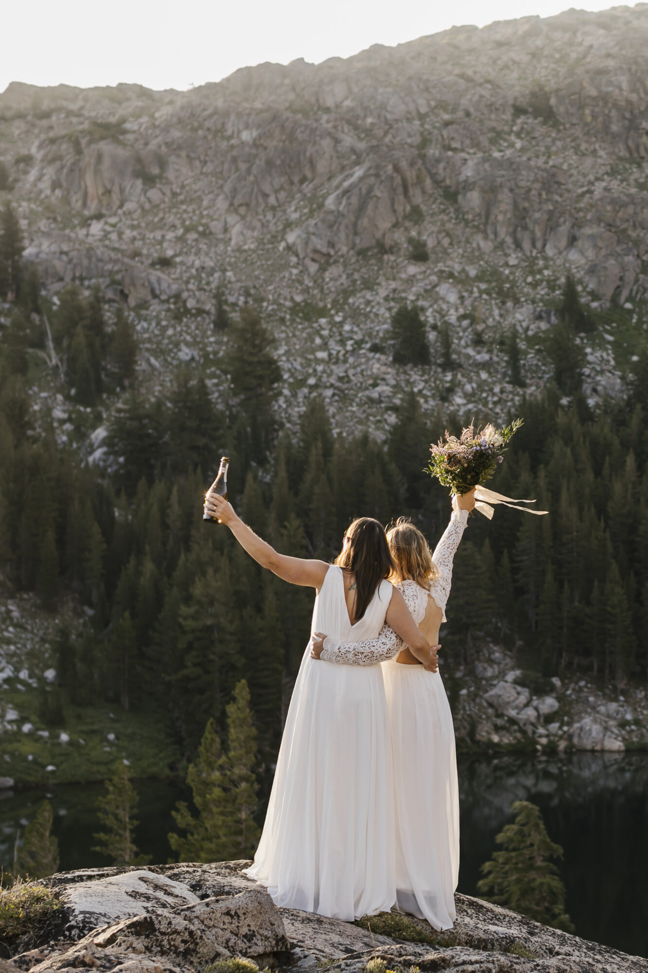 Two brides toast the sunrise with champagne in celebration of their adventurous mountain wedding