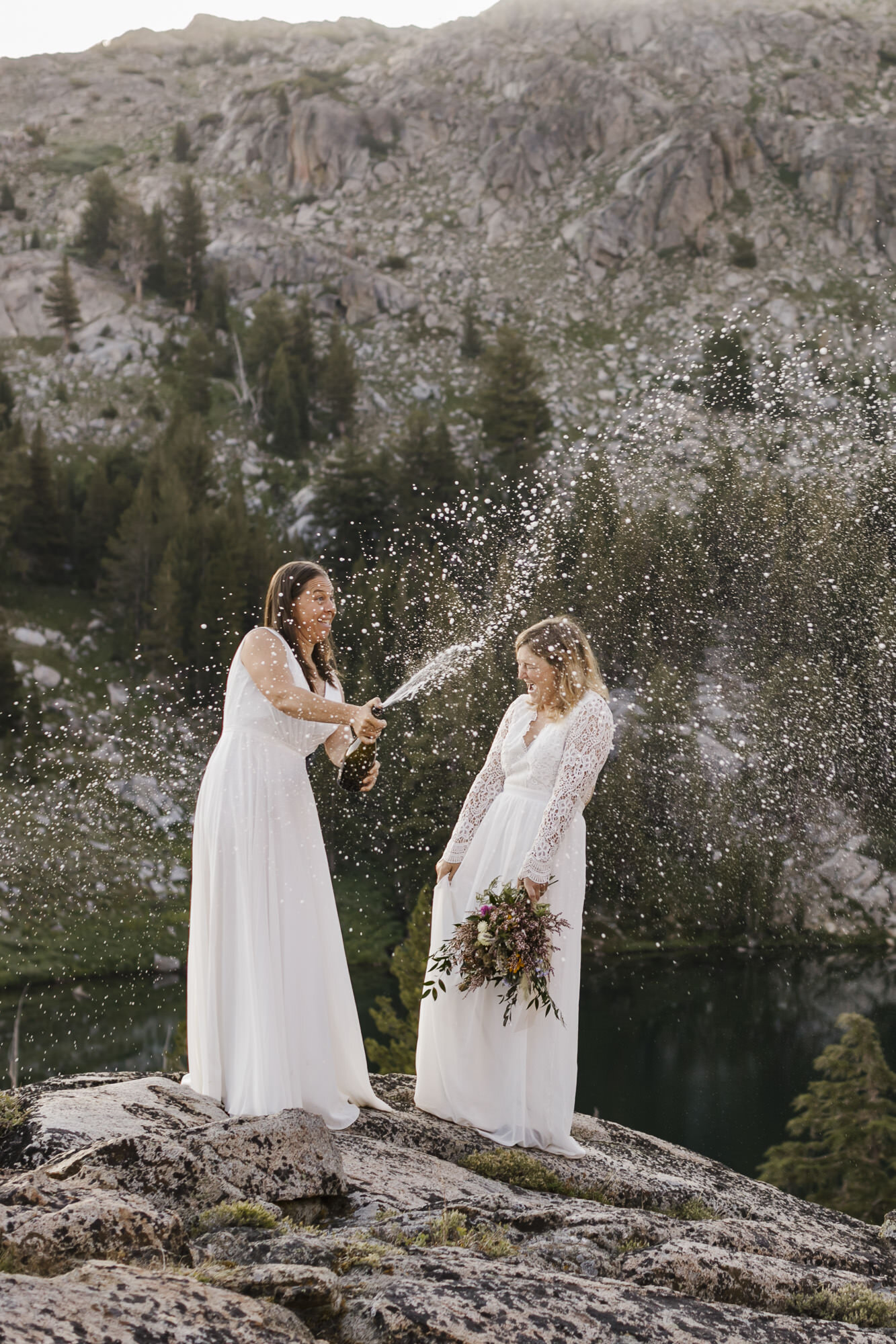Lesbian couple celebrates getting married by popping champagne during their backpacking elopement in the Sierra Nevada mountains in California