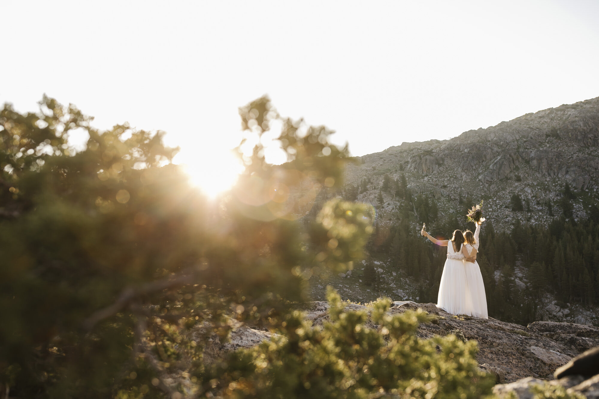 Wedding couple raises their arms in celebration at sunrise during their backpacking elopement
