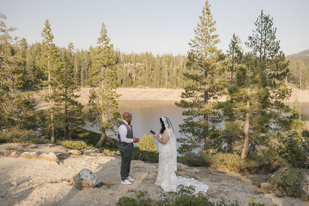 Wedding couple exchange vows in the Tahoe forest with a lake behind them