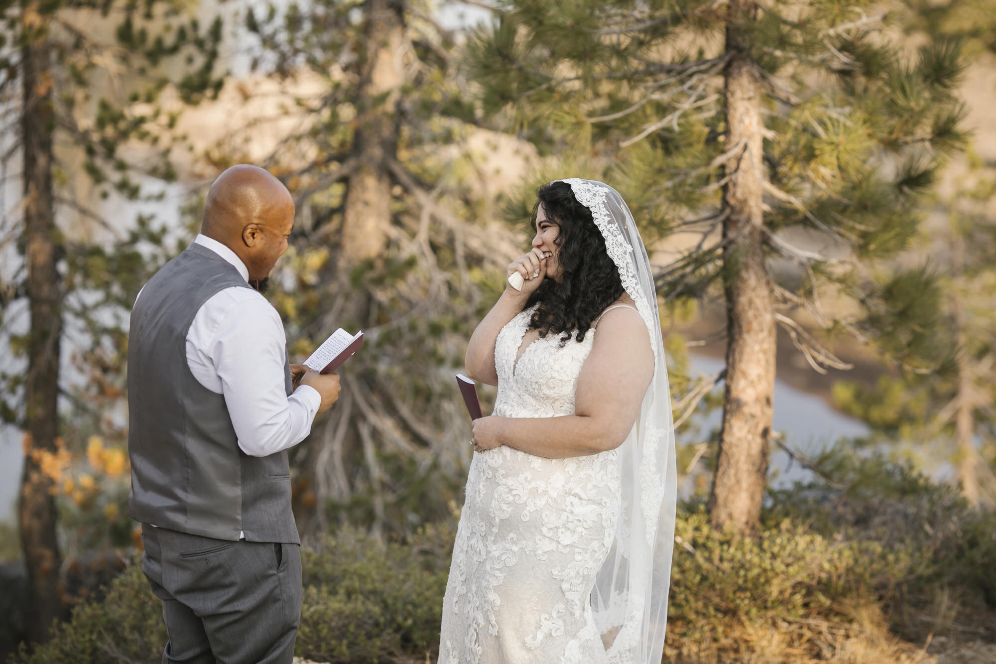 Bride laughs as her groom reads his wedding vows to her in the forest