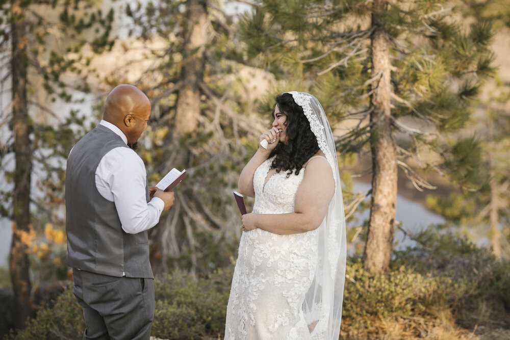 Bride laughs as her groom reads his wedding vows to her in the forest