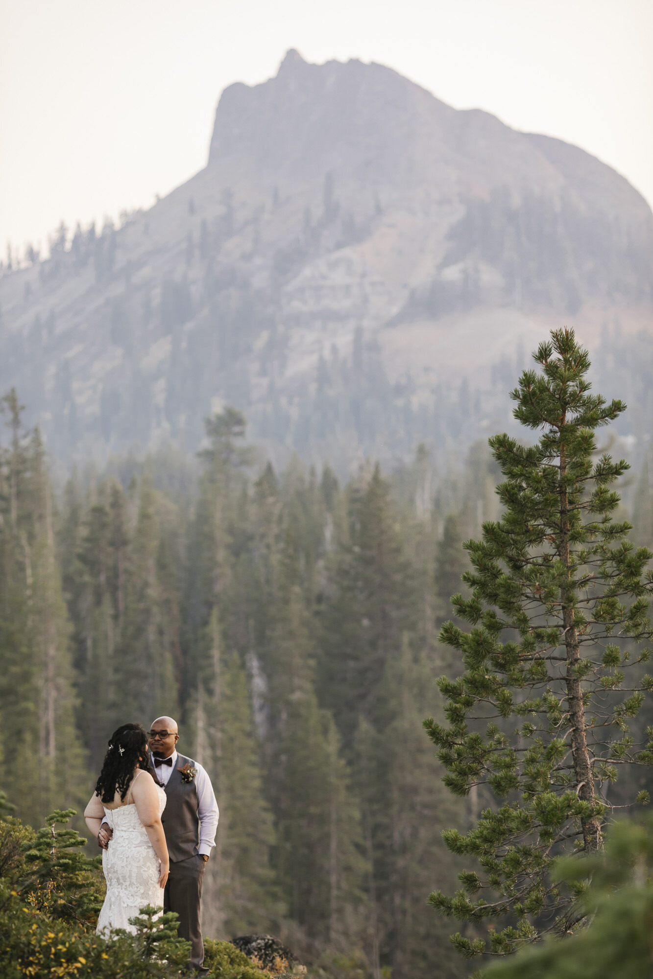Wedding couple stand together in front of mountain peak in Tahoe forest
