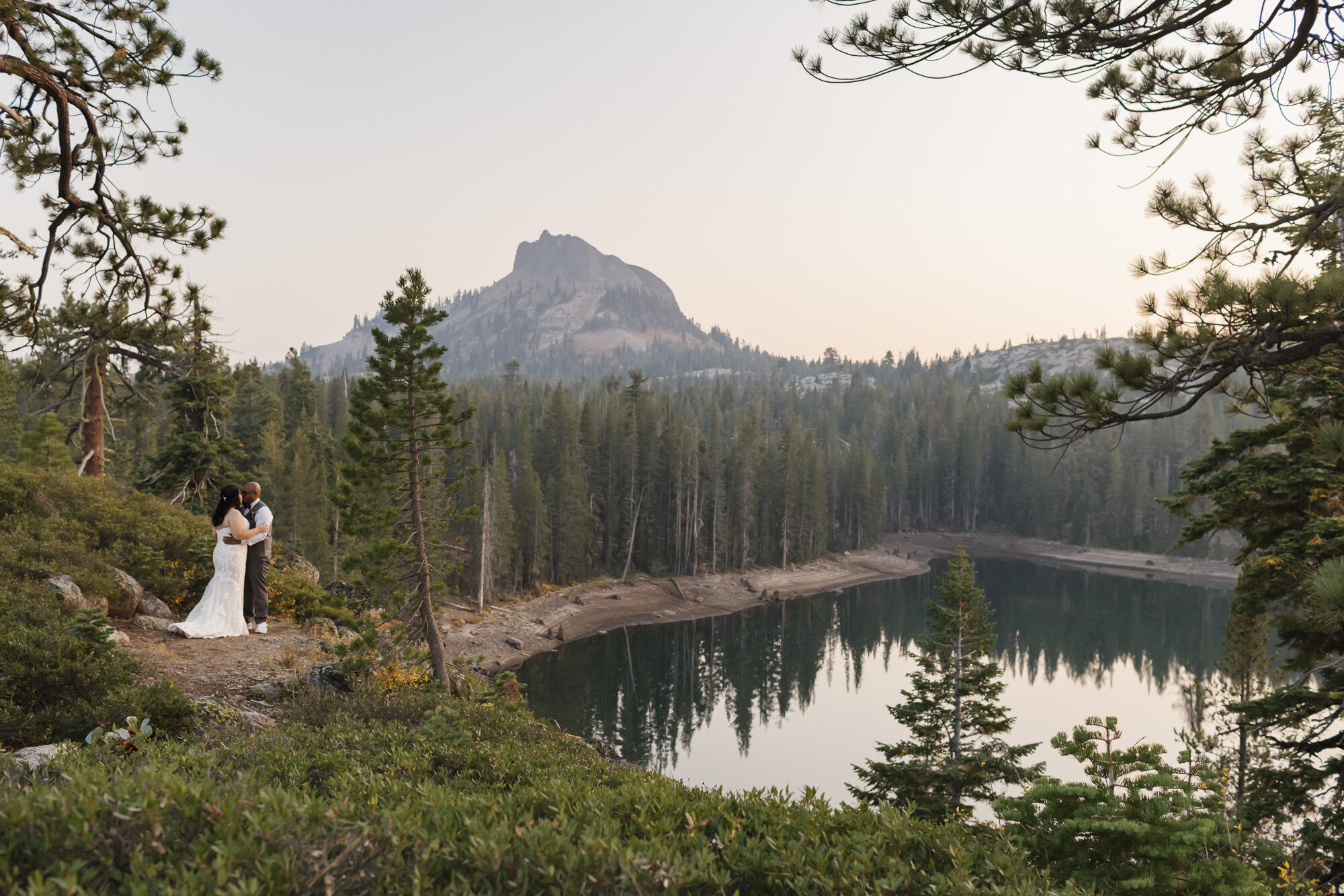 Wedding couple overlook lake and mountain peak in the Tahoe forest