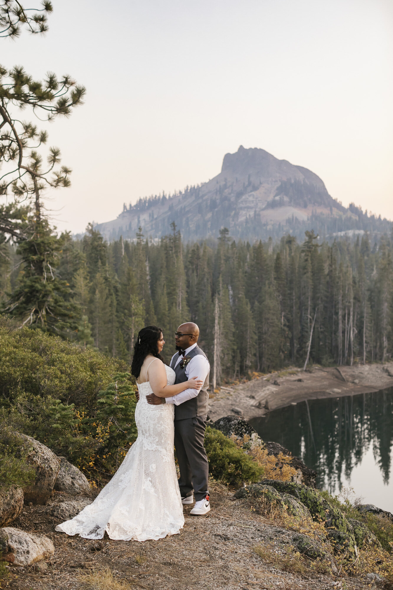 Wedding couple hold each other overlooking lake and mountain peak in Tahoe forest during their adventurous elopement