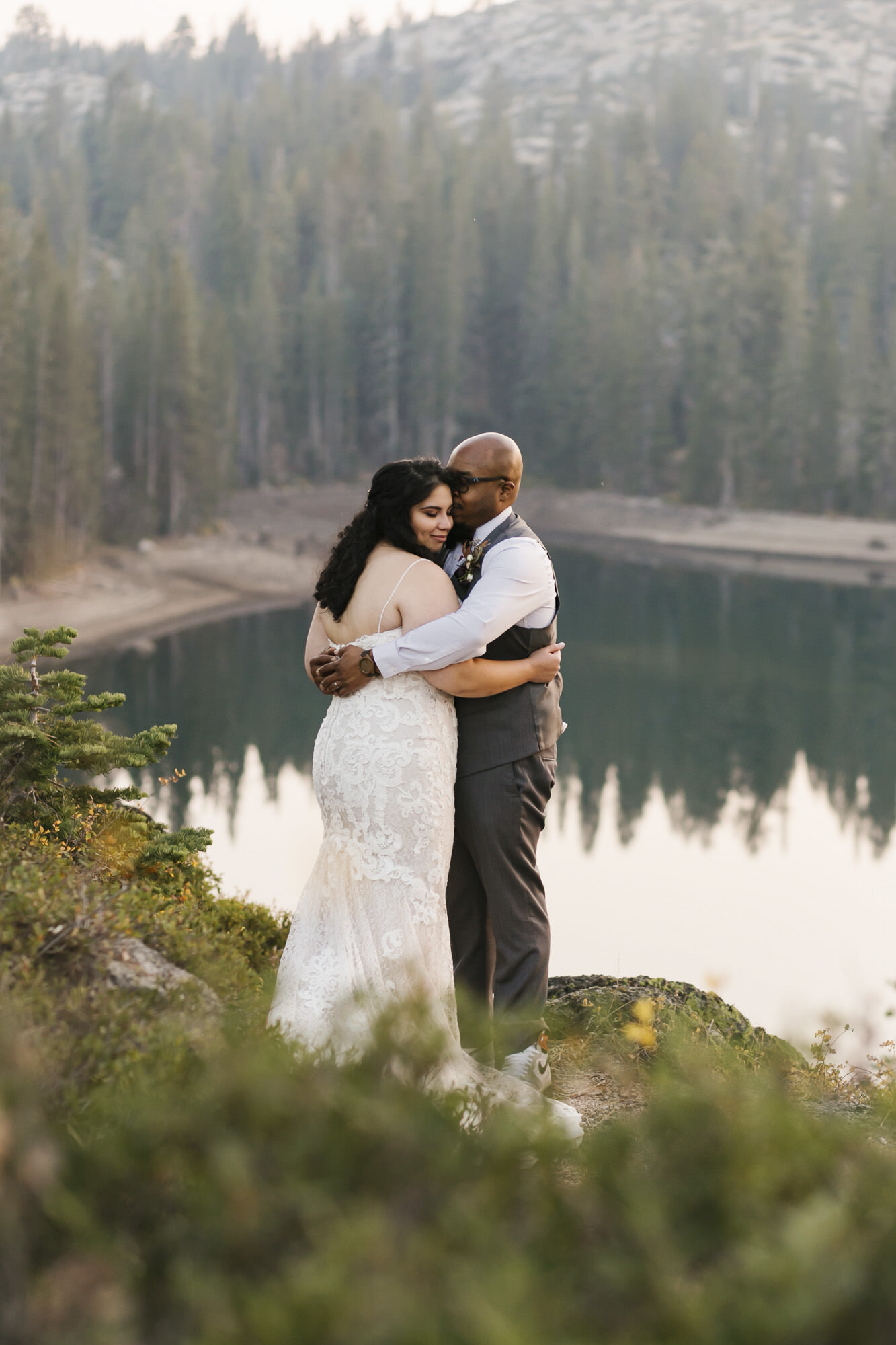 Wedding couple snuggle together at sunset in front of lake in Tahoe forest