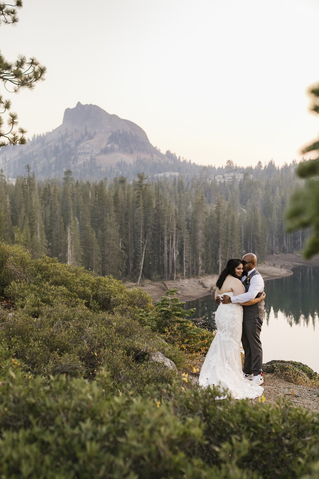 Wedding couple hold each other close with mountain peak in the distance behind them in Tahoe forest