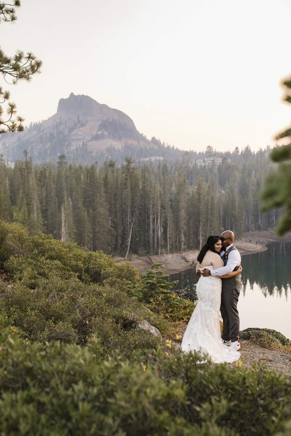 Wedding couple hold each other close with mountain peak in the distance behind them in Tahoe forest