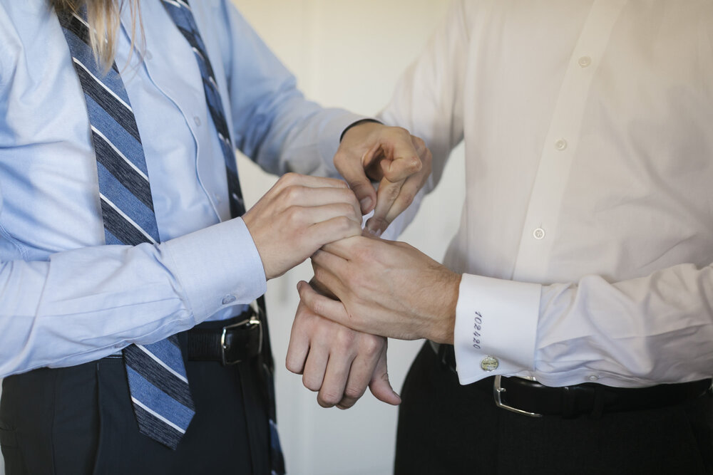 Detail shot of groom's brother helping with his cufflinks on his wedding day getting ready