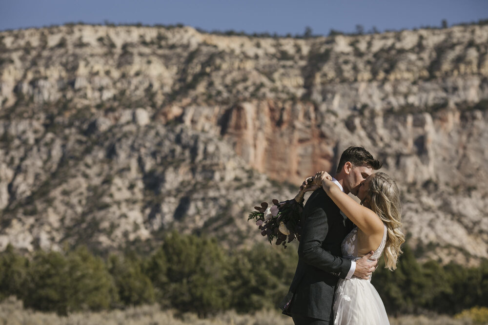 Wedding couple kiss in front of the red cliffs at their Utah Airbnb outside of Zion