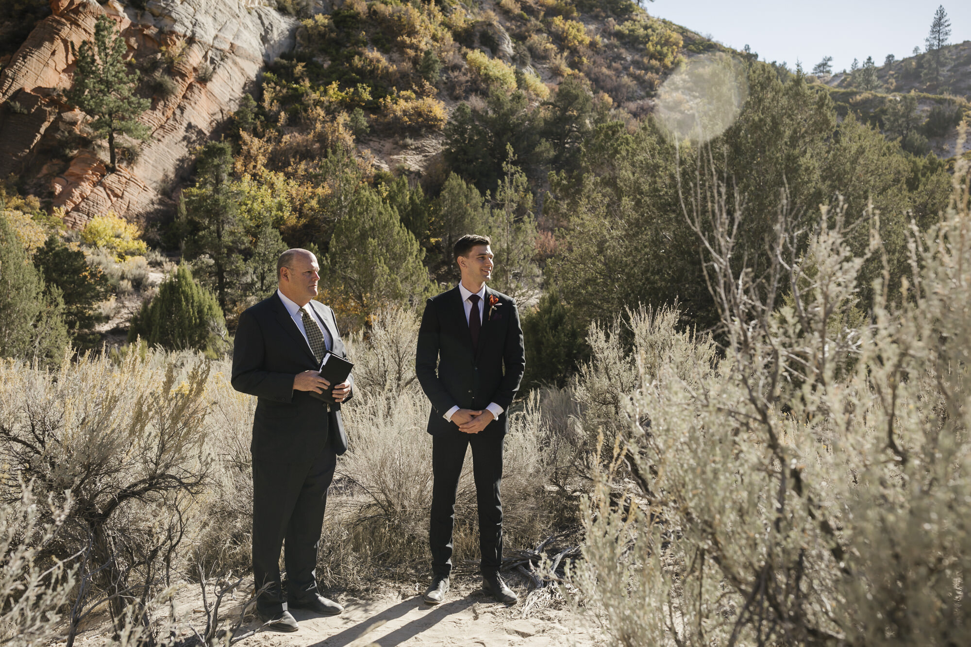 Groom stands outdoors with his ceremony officiant waiting for his bride at his Utah desert wedding
