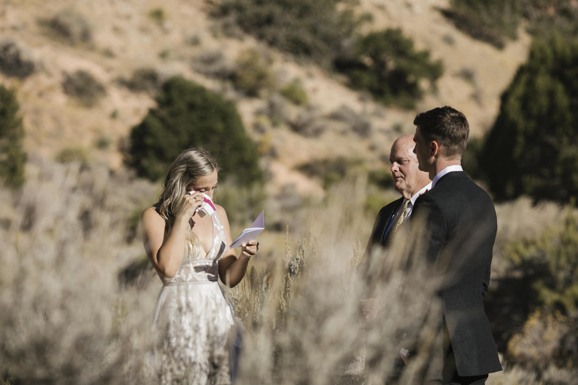Bride wipes her eyes while exchanging vows during her wedding ceremony in the Utah desert