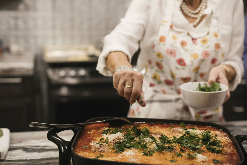 Bride's mother and chef sprinkles parmesan and fresh basil on lasagna