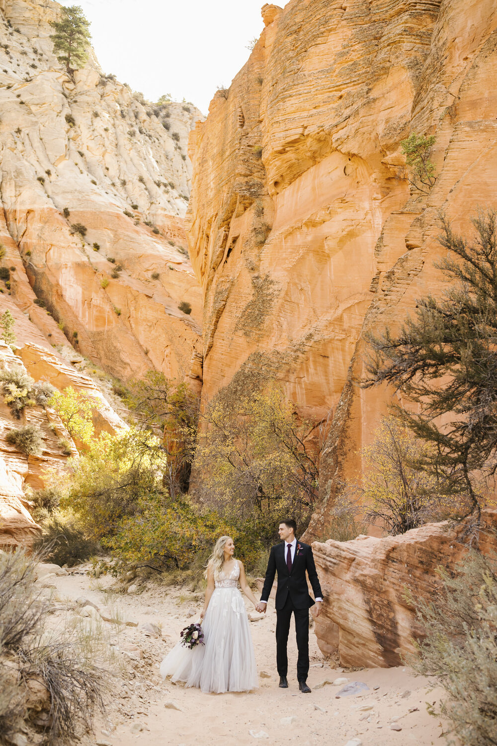 The day after their wedding, a couple walk holding hands for their portraits in the Utah desert