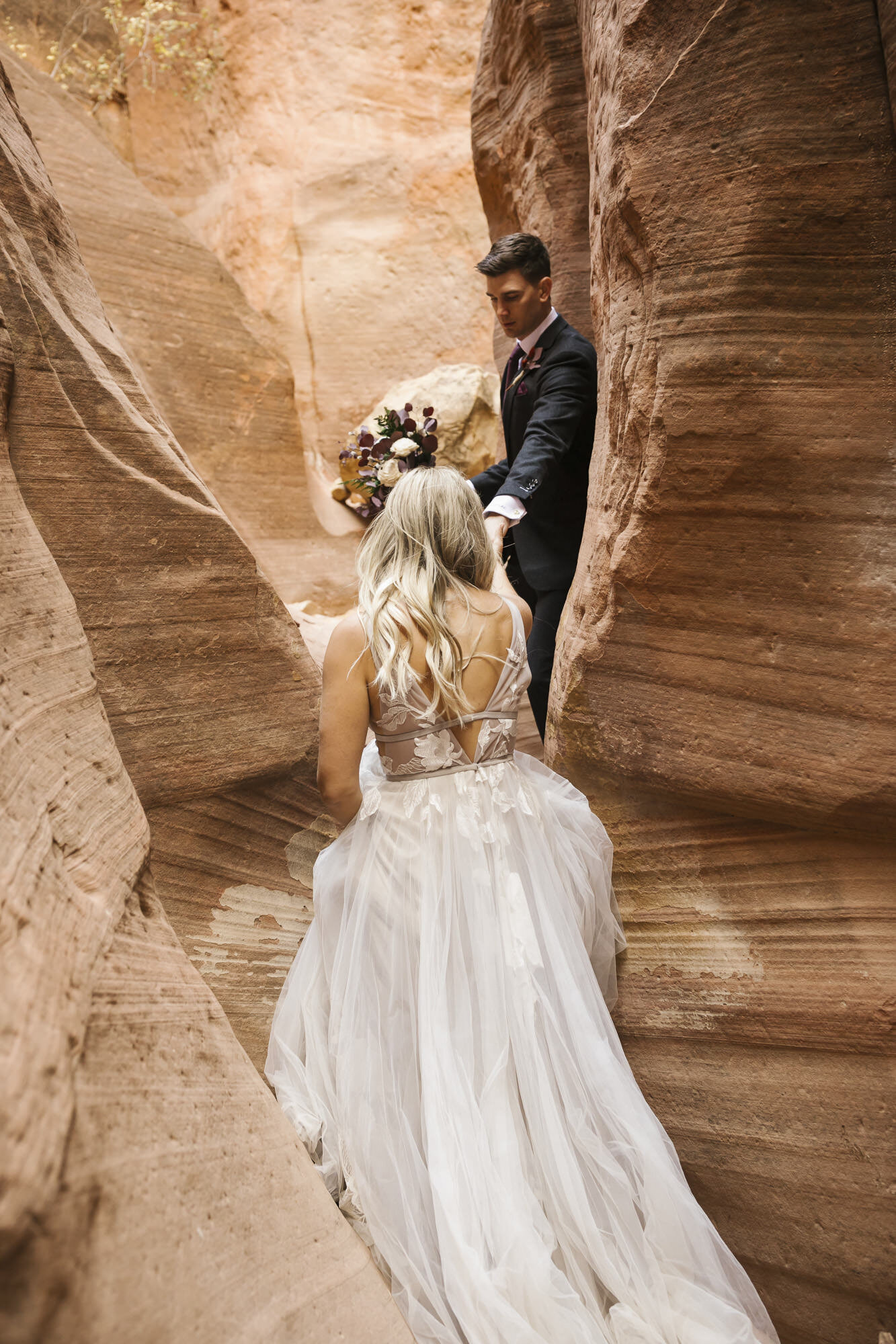 Groom helps his bride walk through slot canyon outside of Zion in Utah