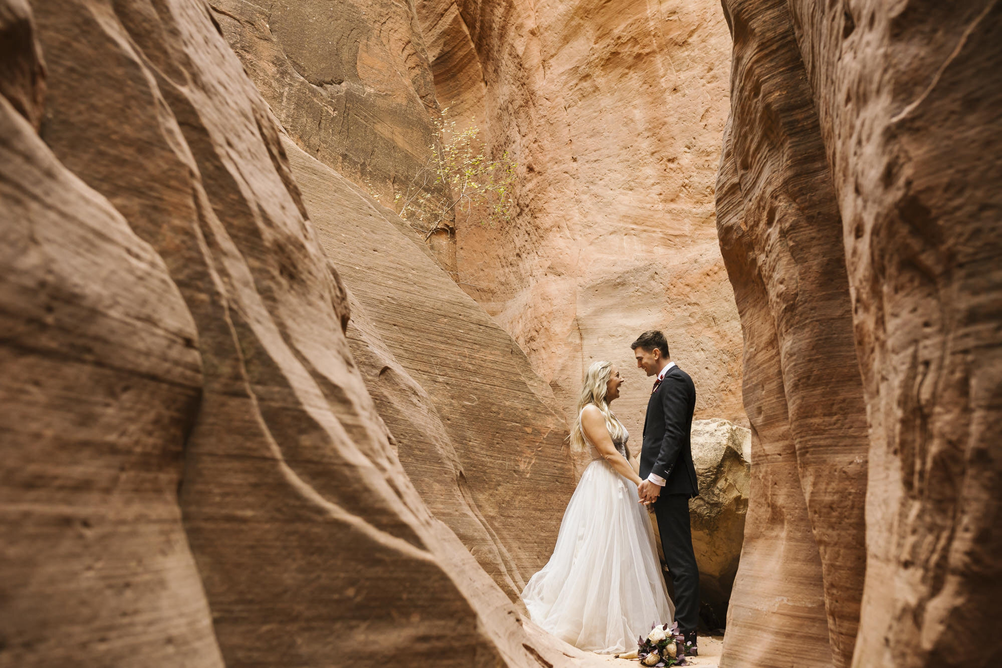 Bride and groom hold hands in a slot canyon in the Utah desert