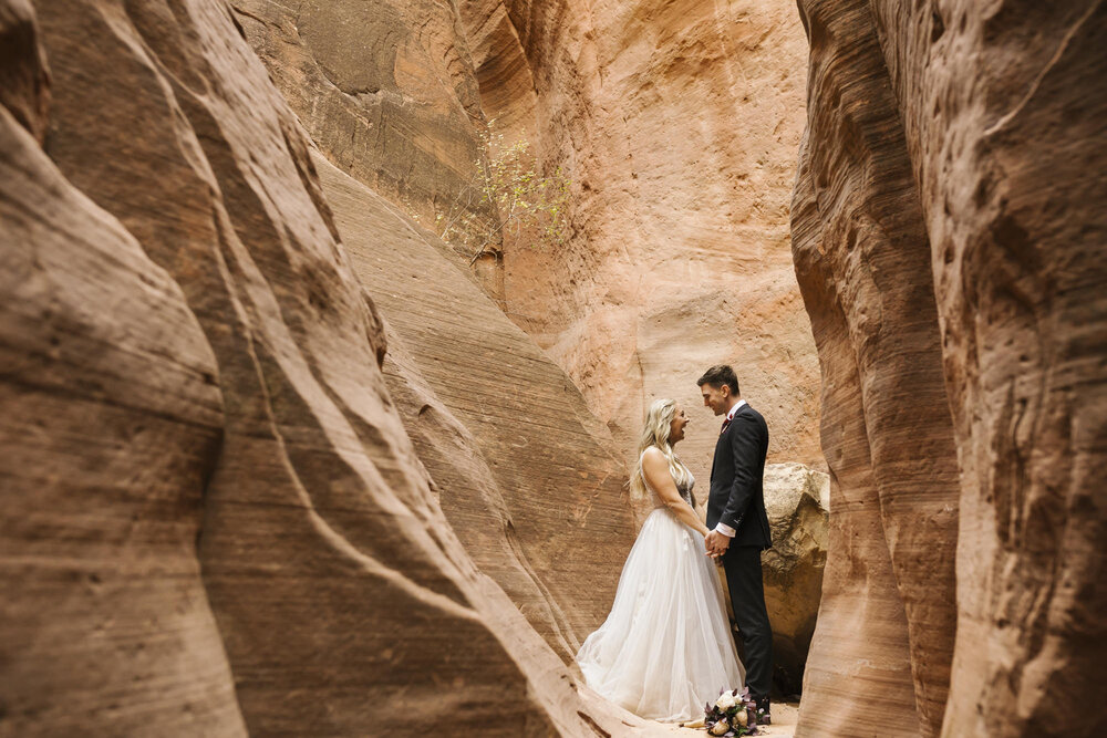 Bride and groom hold hands in a slot canyon in the Utah desert