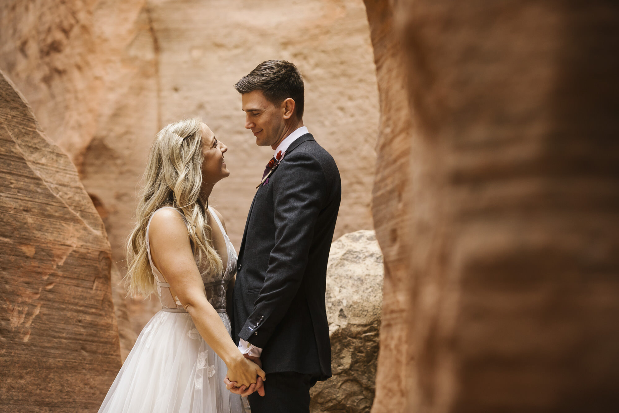 Wedding couple smile at each other while taking their portraits in the Utah desert