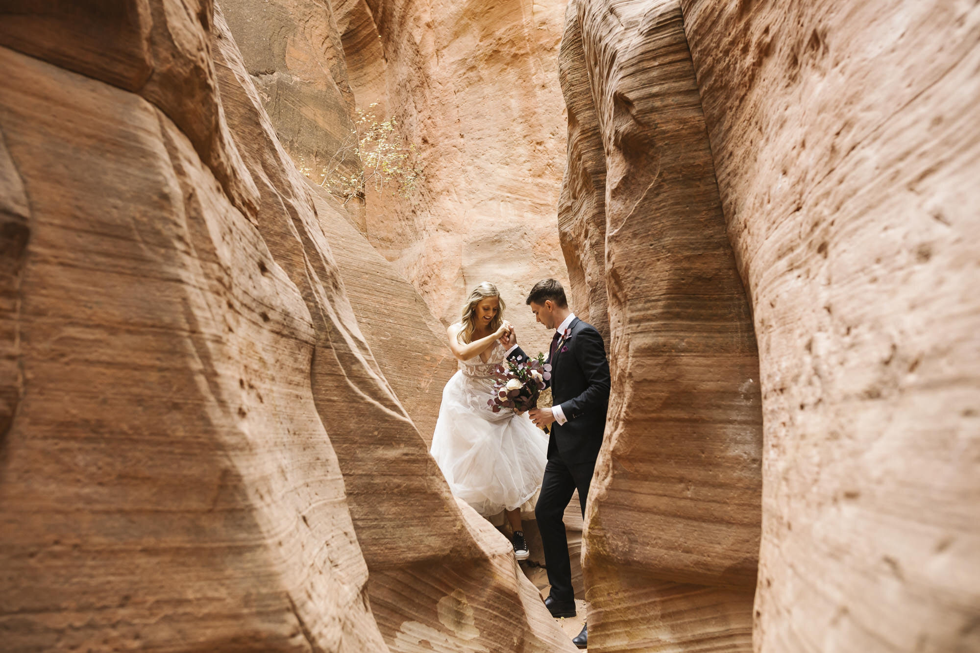 Groom gives his bride a hand as they walk through a slot canyon in Utah