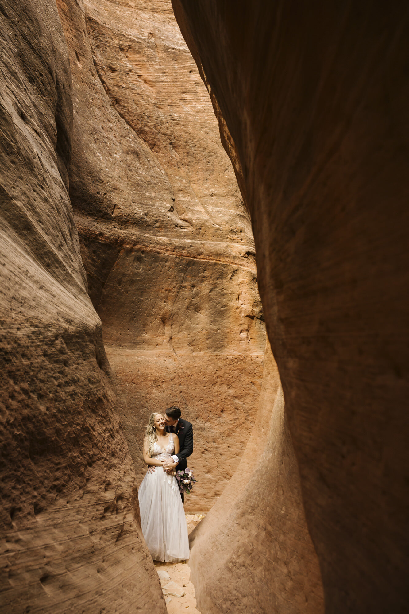 Groom kisses his bride's cheek during their wedding portraits in the Utah desert