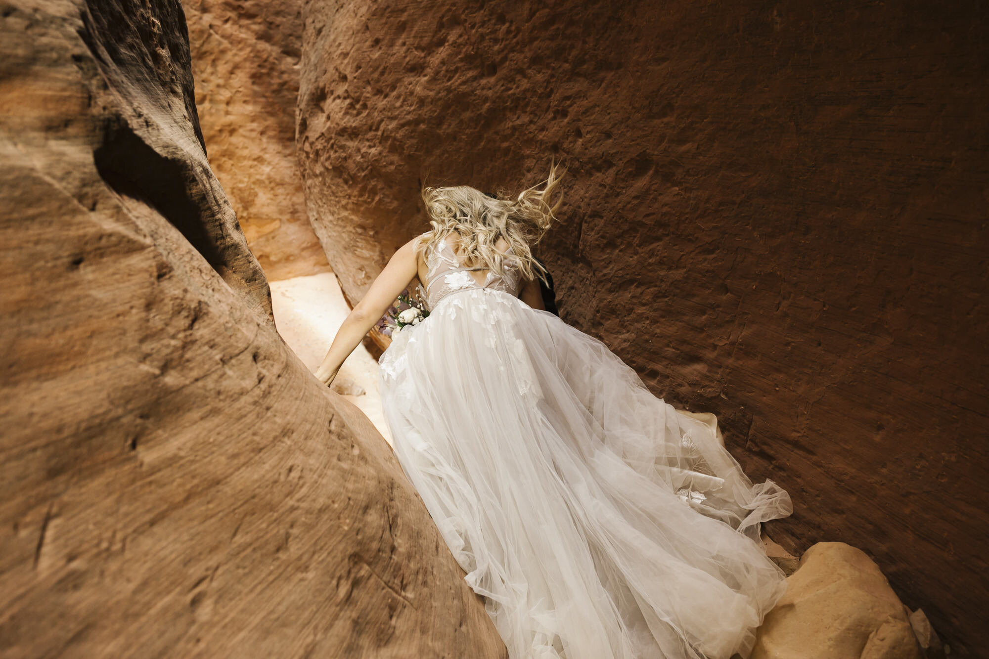 Bride jumps down while navigating a slot canyon in the Utah desert