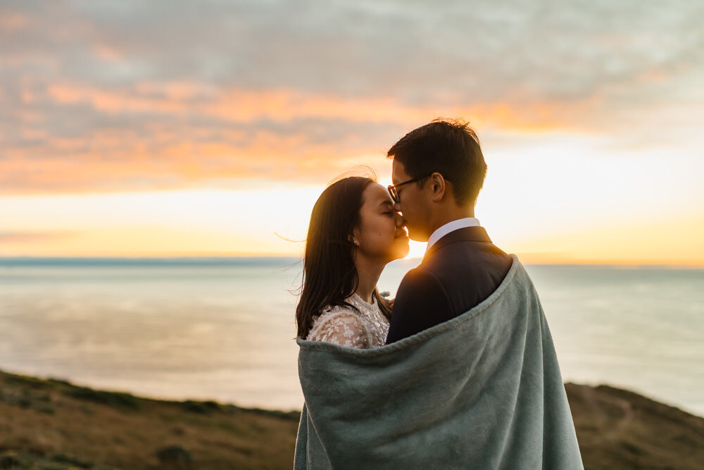 Elopement couple wrap a blanket around themselves at sunset in Point Reyes