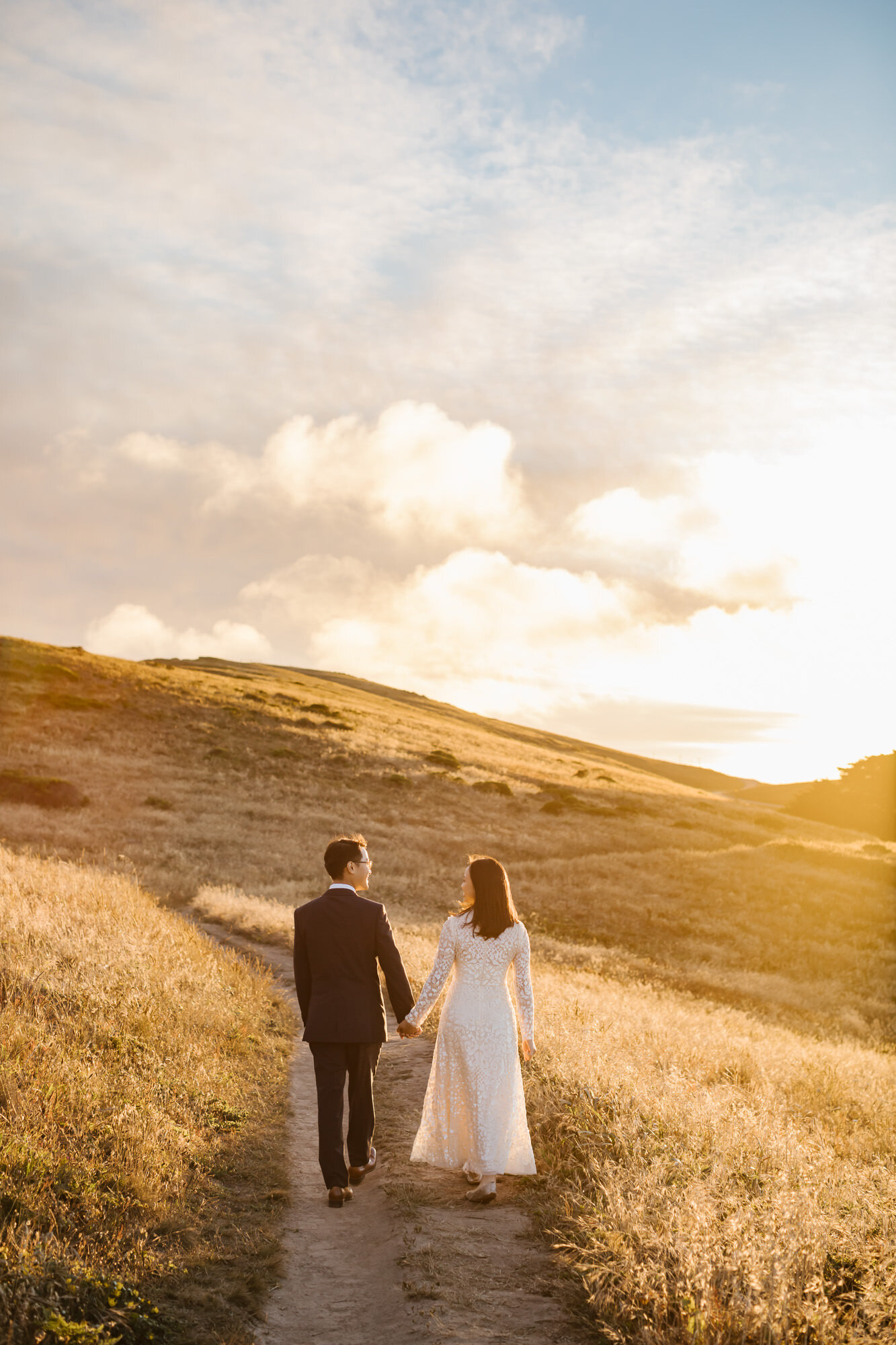Point Reyes elopement couple hold hands and walk down a trail together during golden hour 