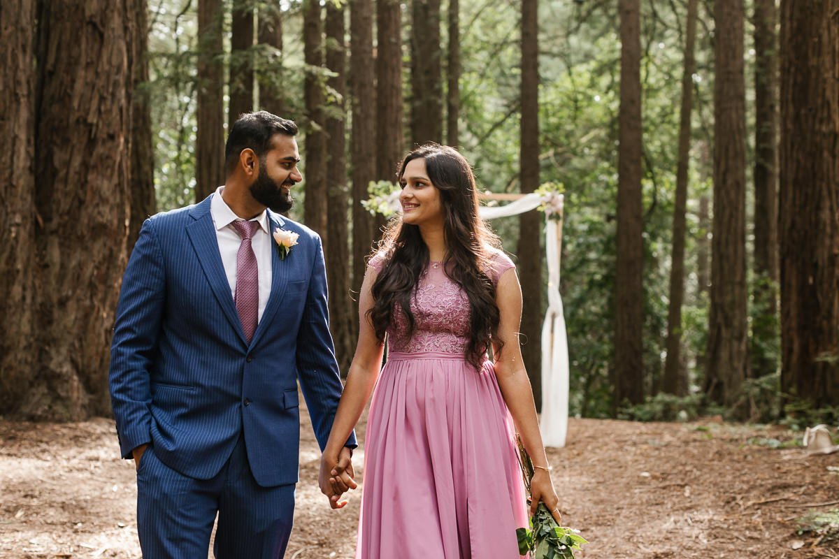 Wedding couple walk in front of their ceremony arch at their redwood forest elopement in Joaquin Miller Park