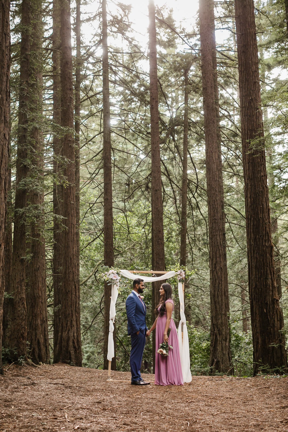 Bride and groom stand in front of their ceremony arch at their redwood forest elopement in Joaquin Miller Park