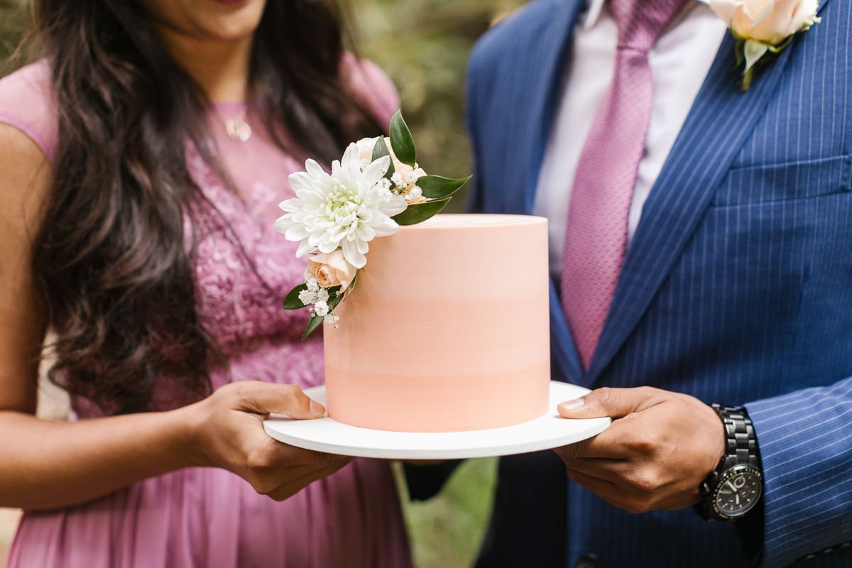Couple hold their pink wedding cake at their redwood forest elopement