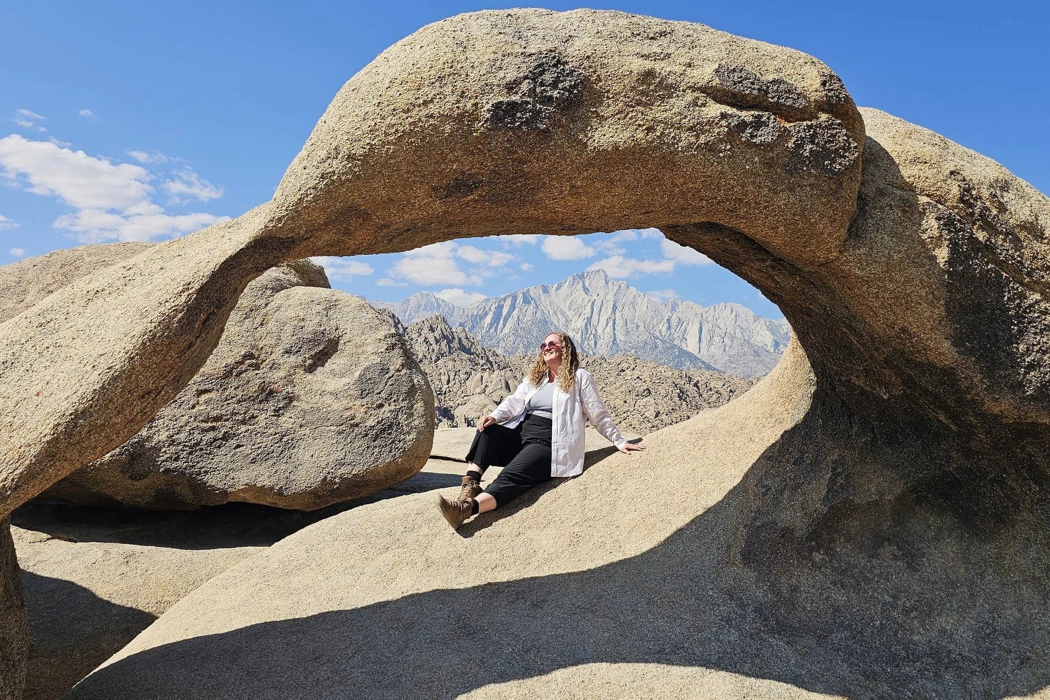 Natalie Pearl sits under the Mobius Arch rock formation with Mount Whitney behind her