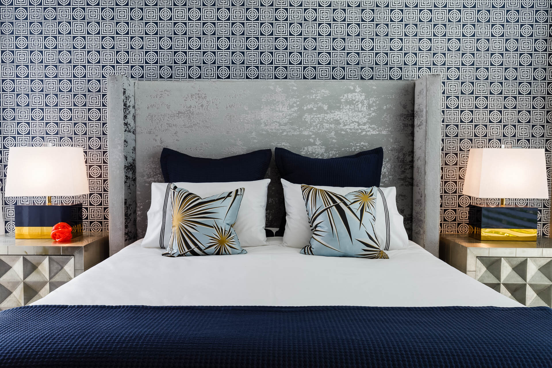 Luxury bedroom at Mathieson Residence in Mosman featuring a custom upholstered bed, geometric wallpaper, mirrored bedside tables and layered blue and white furnishings.