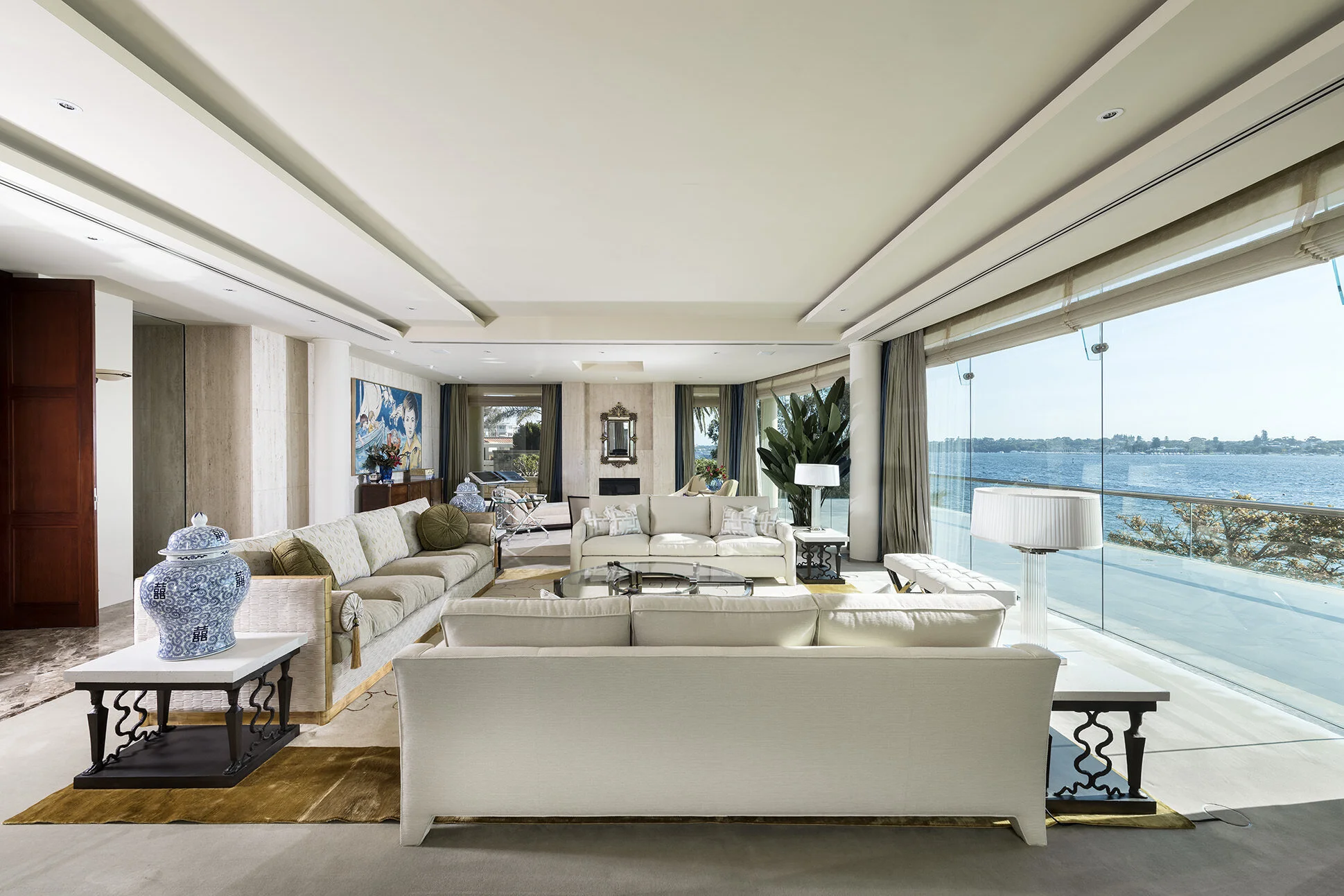 Open-plan luxury living room at Watkins Residence featuring bespoke furnishings, floor-to-ceiling glazing and panoramic waterfront views, creating a sophisticated indoor-outdoor lifestyle experience.